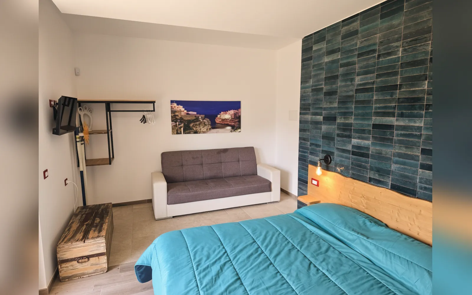 La camera con il letto dal copriletto turchese, il divano e la parete di piastrelle blu